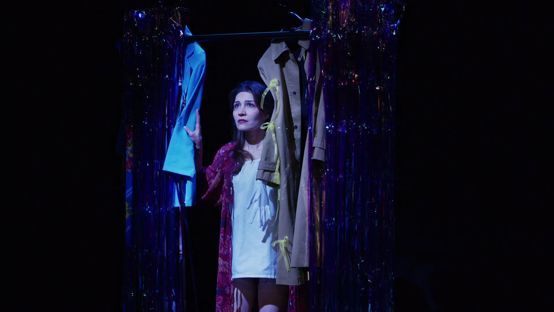 Dahlia standing quietly among costumes and shimmering curtains